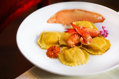 A plate of lobster ravioli garnished with lobster pieces and edible flowers, served with a slice of fish.