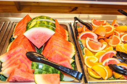 A buffet display featuring sliced watermelon and a variety of citrus fruits, including oranges and grapefruits.