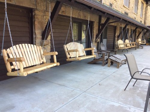 A row of wooden swings and chairs on a porch with stone walls in the background.