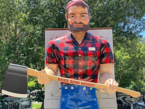 A large statue of a lumberjack in a plaid shirt holding an axe, with "River Bend Resort" on the axe handle.