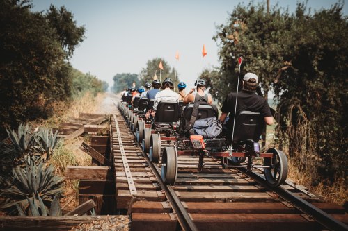 A group of people riding on pedal-powered carts along a wooden railway track surrounded by greenery.