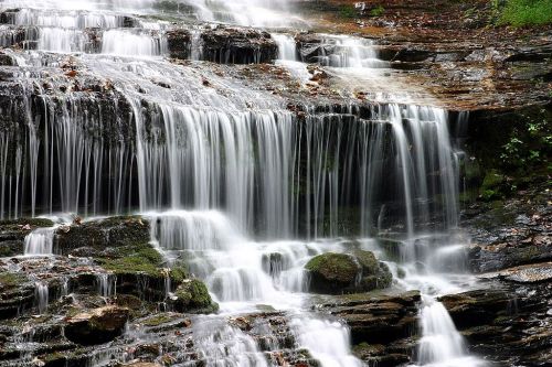 A serene waterfall cascading over moss-covered rocks, surrounded by lush greenery.
