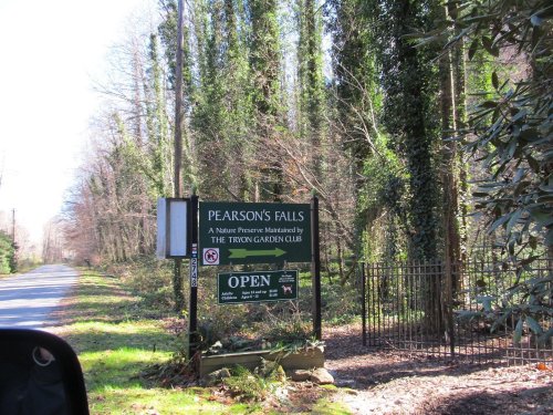 Sign for Pearson's Falls Nature Preserve, surrounded by trees and greenery, with an open hours notice.