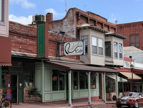 A charming café with a vintage sign, surrounded by historic buildings and shops in a quaint town.