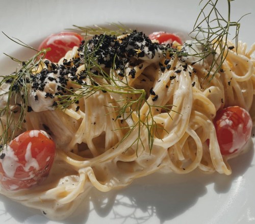 A plate of spaghetti topped with cherry tomatoes, creamy sauce, and garnished with herbs and black seasoning.