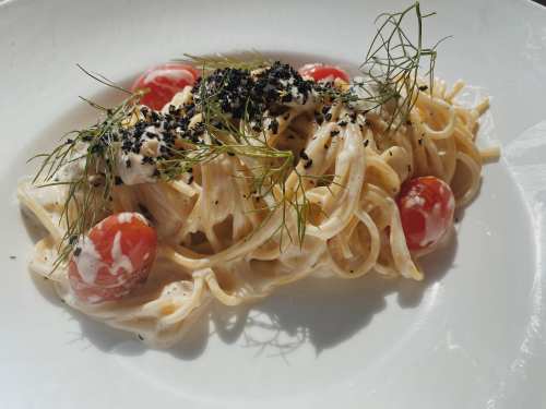 A plate of creamy pasta with cherry tomatoes, topped with herbs and black seasoning.