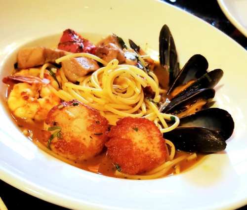 A plate of seafood pasta featuring shrimp, scallops, mussels, and vegetables in a rich sauce.