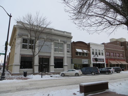 Snow-covered street scene featuring historic buildings and parked cars.