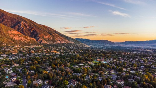 Aerial view of a valley surrounded by mountains, showcasing a residential area and lush greenery at sunset.