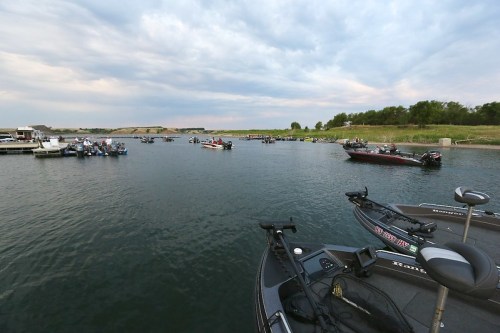 A scenic view of a lake filled with fishing boats under a cloudy sky, with grassy banks in the background.