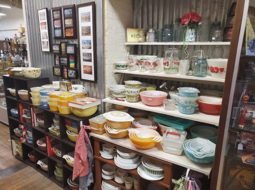 A display of vintage kitchenware, including bowls, jars, and dishes, arranged on shelves in a cozy shop.