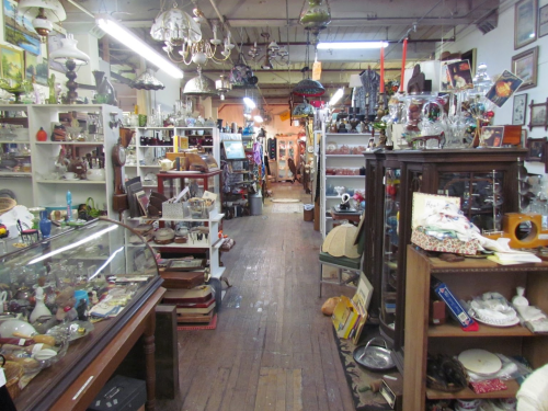 A narrow aisle in an antique shop filled with various collectibles, lamps, and vintage items on display.