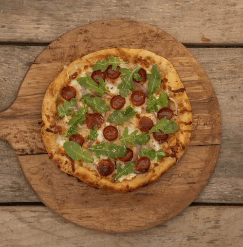 A freshly baked pizza topped with pepperoni and arugula on a wooden serving board.