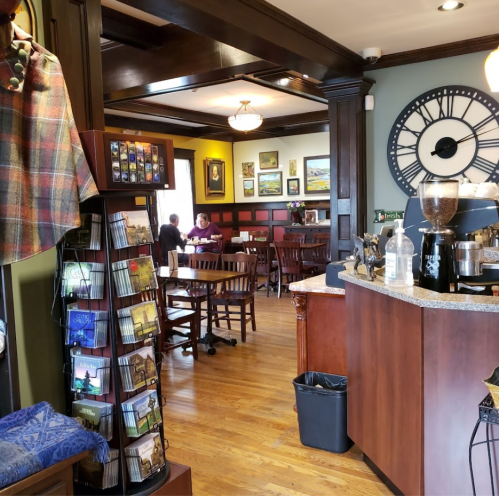 Cozy café interior with wooden furniture, a clock, and artwork on the walls, featuring a coffee counter and patrons.