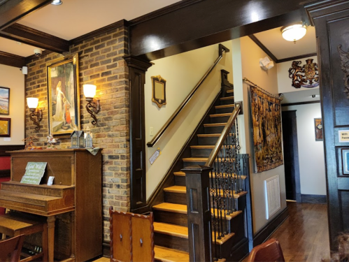 A cozy interior featuring a staircase, brick wall, wooden accents, and artwork, with a piano in the foreground.