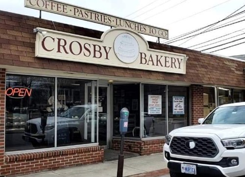 A bakery storefront with a sign reading "Crosby Bakery," featuring an open sign and a parked white truck outside.
