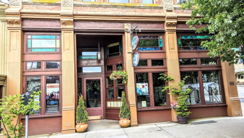 Historic building facade with large windows, decorative trim, and potted plants at the entrance.