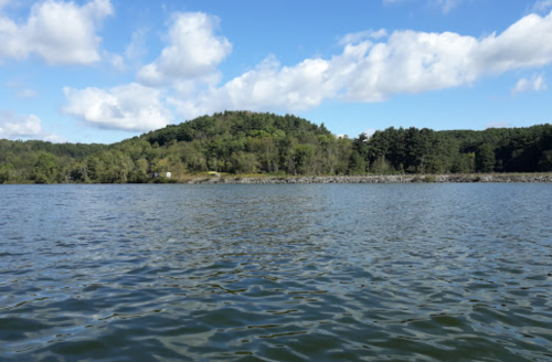 A serene lake scene with gentle waves, surrounded by green hills and a blue sky with fluffy clouds.