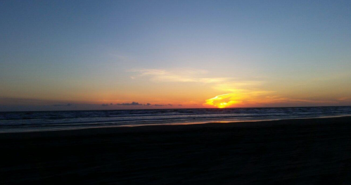 A serene beach at sunset, with vibrant colors reflecting on the water and a clear sky.