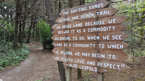 Wooden sign in a forest with text about land as a community, alongside a nature trail path.
