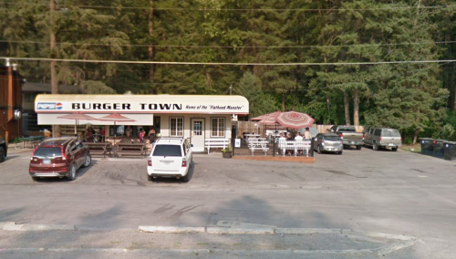 A small burger restaurant named "Burger Town" with outdoor seating, surrounded by trees and parked cars.