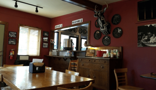 Cozy restaurant interior with wooden tables, a service counter, and decorative wall plates. Warm, inviting atmosphere.