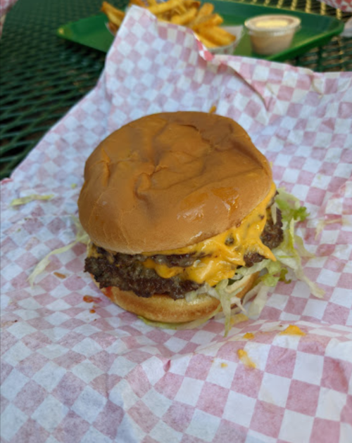 A cheeseburger with melted cheese and lettuce on a bun, served on a checkered paper with fries in the background.