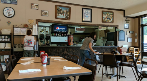 A cozy diner interior with two staff members cleaning tables and a soda fountain in the background.