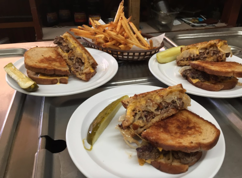 Three plates of sandwiches with grilled meat and cheese, served with pickles and a side of crispy fries.