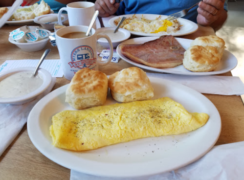 A breakfast spread featuring an omelet, biscuits, ham, coffee, and sides on a wooden table.