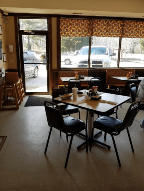 A cozy diner interior with empty tables, chairs, and a view of a parking lot through large windows.