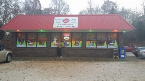 A small pizza restaurant with a red roof, open sign, and festive window decorations. A person stands outside.