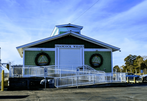 A green building with a white entrance, decorated with wreaths, at Onancock Wharf under a clear blue sky.