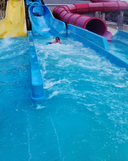 A child splashes in a water slide pool, surrounded by colorful slides and flowing water.