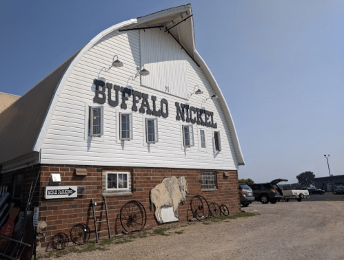A barn with "Buffalo Nickel" painted on the side, featuring a bison mural and vintage wheels in front.