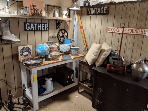 A cozy vintage shop display featuring various antiques, decor items, and a wooden table with a globe and baskets.