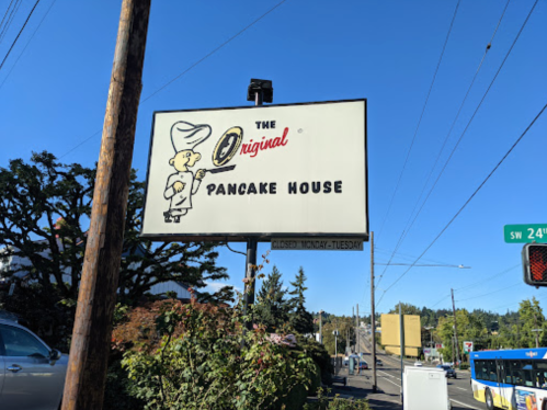 Sign for "The Original Pancake House" with a cartoon chef, indicating it's closed Monday and Tuesday. Clear blue sky.