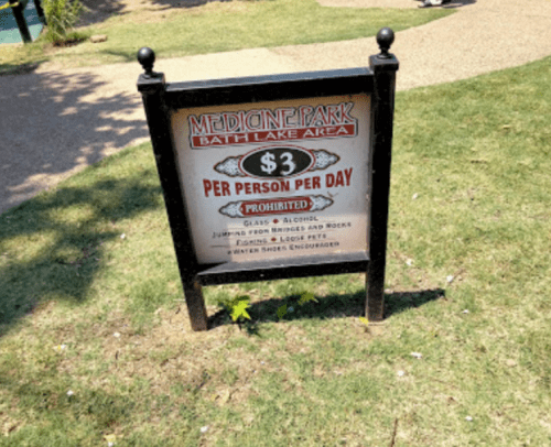 Sign at Medicine Park Bath Lake Area stating $3 per person per day, with rules against glass, jumping, and running.