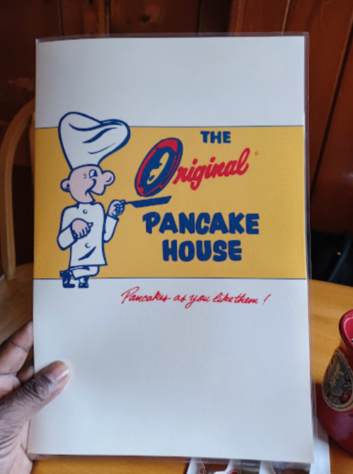 A hand holding a menu from The Original Pancake House featuring a cartoon chef and the slogan "Pancakes as you like them!"