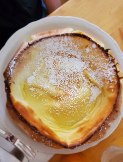 A round, fluffy pancake topped with powdered sugar, served on a white plate.