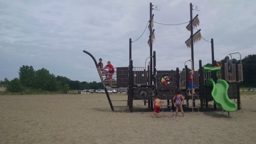 Children playing on a large pirate-themed playground structure on a sandy area, with slides and climbing features.