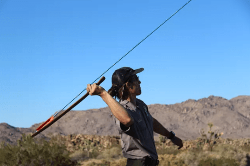 A person in a cap throws a fishing rod against a clear blue sky with mountains in the background.