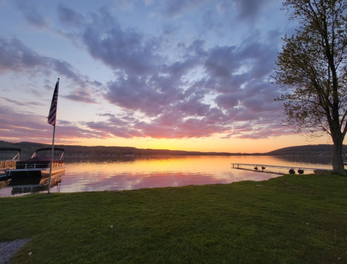A serene lakeside view at sunset, with colorful clouds reflecting on the water and a boat docked nearby.