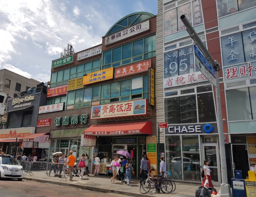 A busy street scene featuring a multi-story building with various signs, shops, and people walking outside.