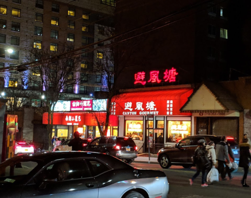A brightly lit restaurant at night with red signage, surrounded by cars and pedestrians in an urban setting.