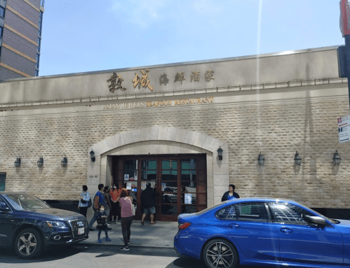 Exterior of a seafood restaurant with a stone facade, large windows, and people walking by on a sunny day.