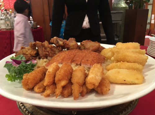 A platter of fried chicken, crispy fish, and golden cassava, garnished with greens, served at a festive gathering.