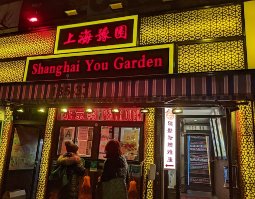 A brightly lit restaurant facade with the sign "Shanghai You Garden" and colorful decorations in a bustling area.