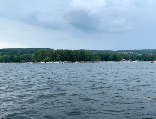 A serene lake scene with boats and a wooded island under a cloudy sky.