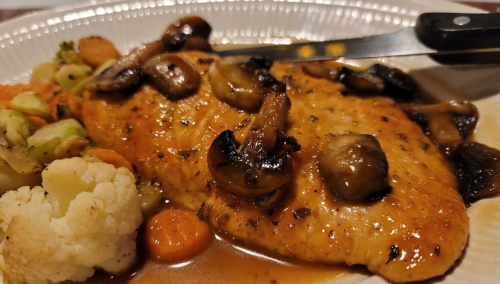 A plate of sautéed chicken breast topped with mushrooms, served with mixed vegetables including cauliflower and carrots.